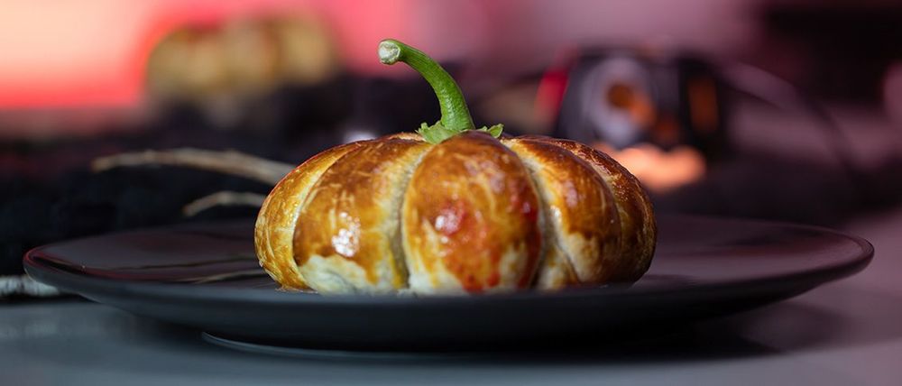 Golden pumpkin-shaped chicken and cheddar pastry on a dark plate