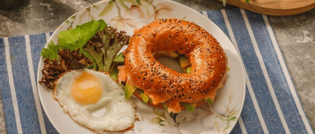 Seeded salmon and avocado bagel served with a fried egg and salad leaves on a plate