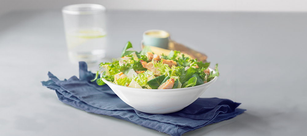 Mixed salad with leafy greens in a white bowl on a blue cloth