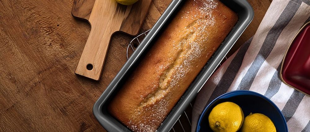 Freshly baked lime cake in a rectangular tin beside citrus fruit